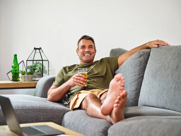 Un homme heureux seul sur son canapé un verre à la main.