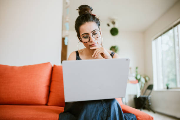 Jeune femme réfléchit sur son ordinateur portable.